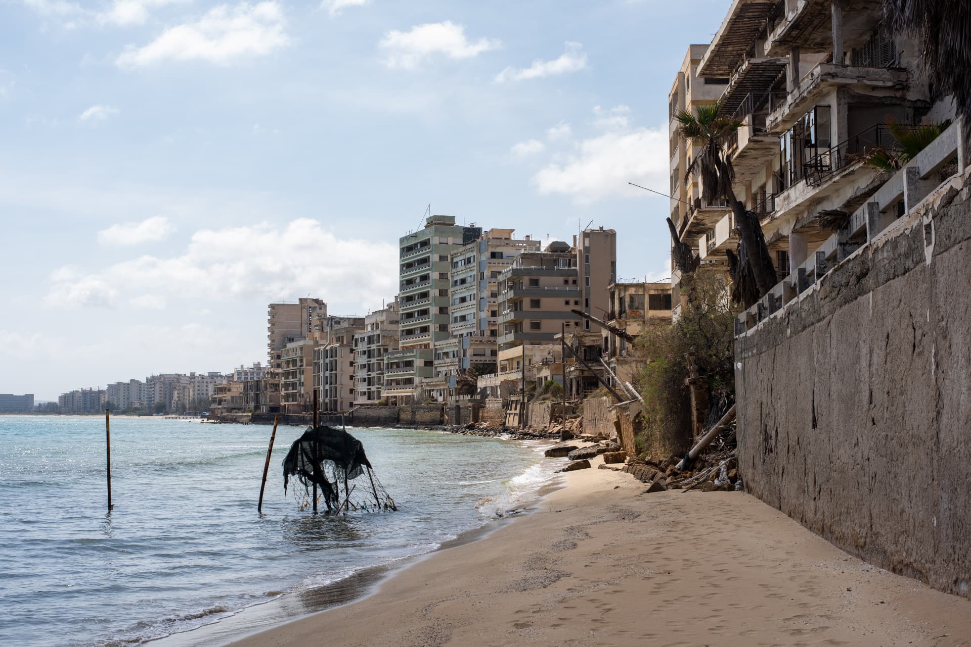 Abandoned coastal buildings lining a quiet sandy beach under a bright sky