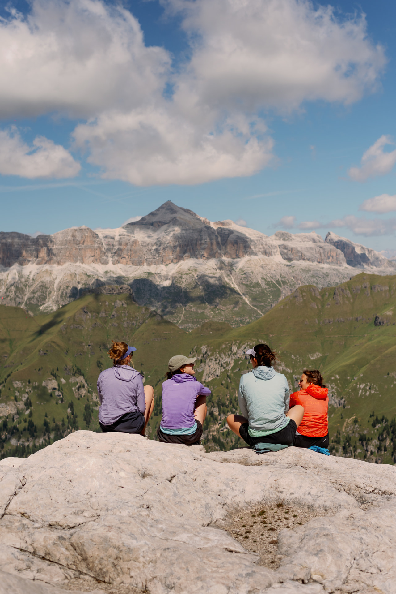 Four hikers sitting on a rocky ridge looking out at the dramatic peaks of the Dolomites