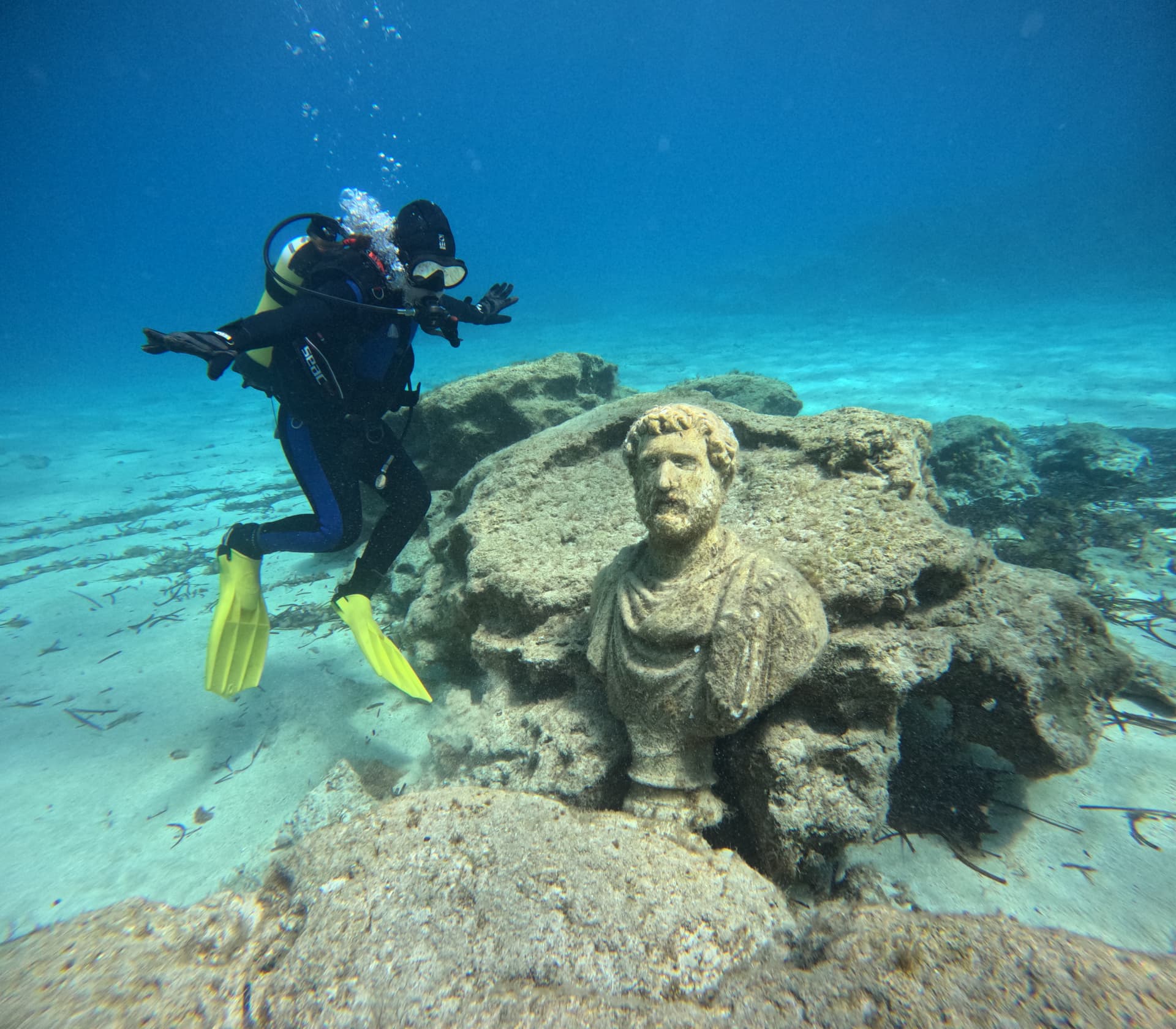 Scuba diver swimming near an ancient underwater statue in clear blue water